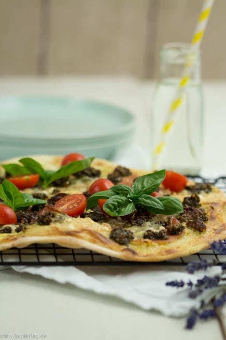 Flammkuchen mit Serranoschinken, Pesto, getrockneten und frischen Tomaten, Basilikum und Parmesan.