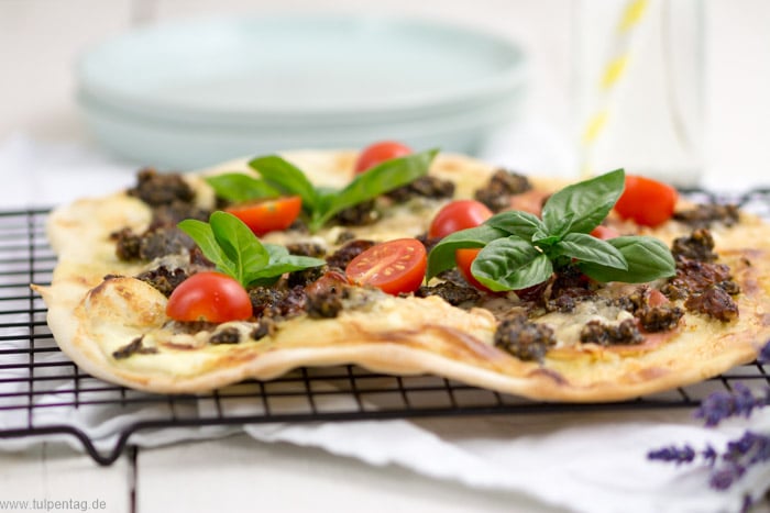 Flammkuchen mit Serranoschinken, Pesto, getrockneten und frischen Tomaten, Basilikum und Parmesan.